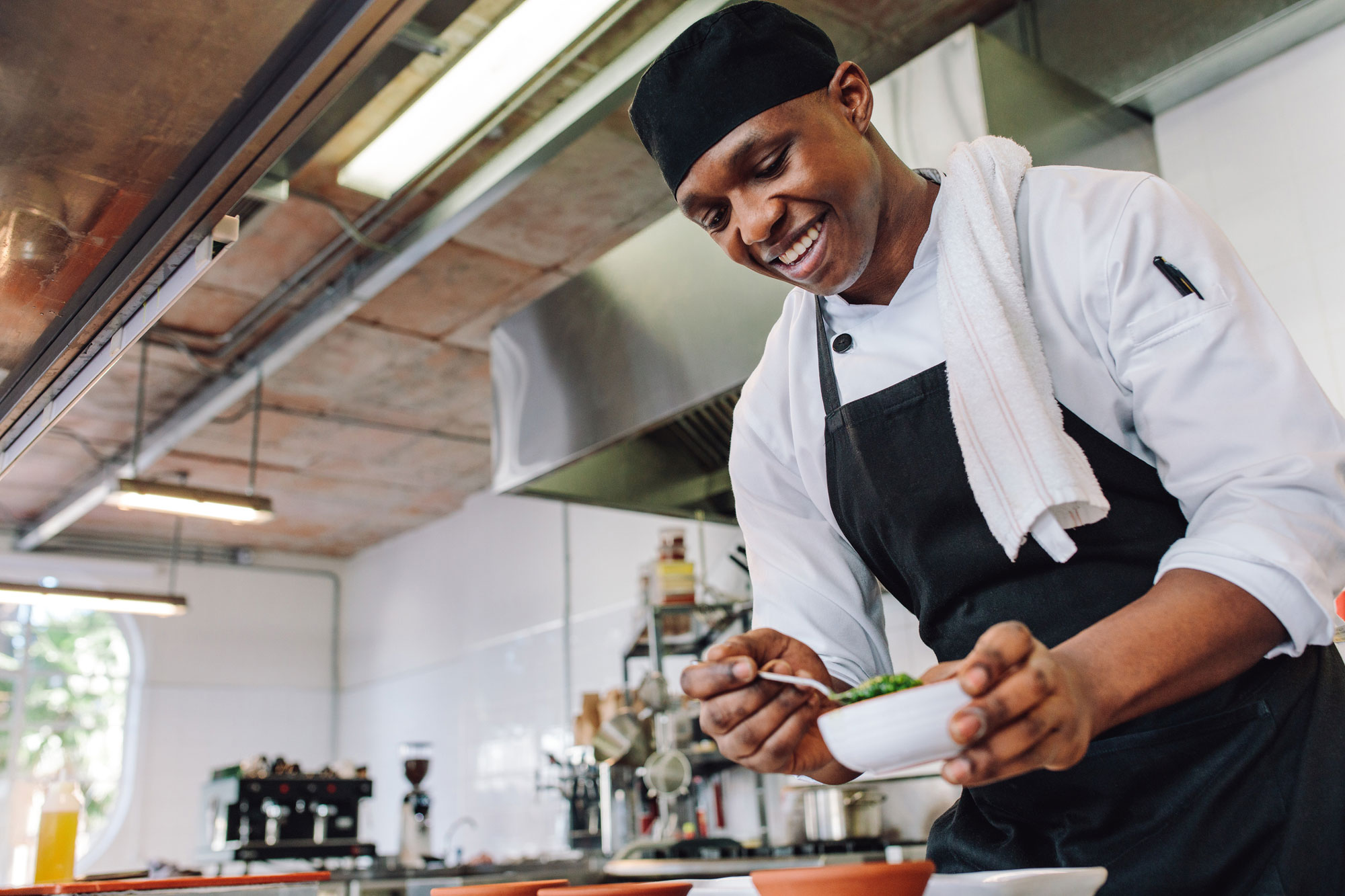 Happy male cook wearing apron standing by kitchen counter preparing food.