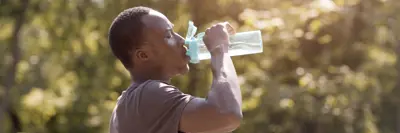 Man drinking from large water bottle outdoors in the summer.