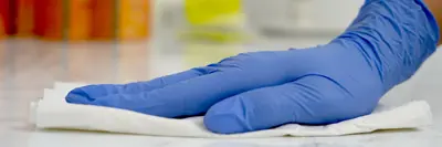 Close-up of a person disinfecting a surface while wearing a glove.